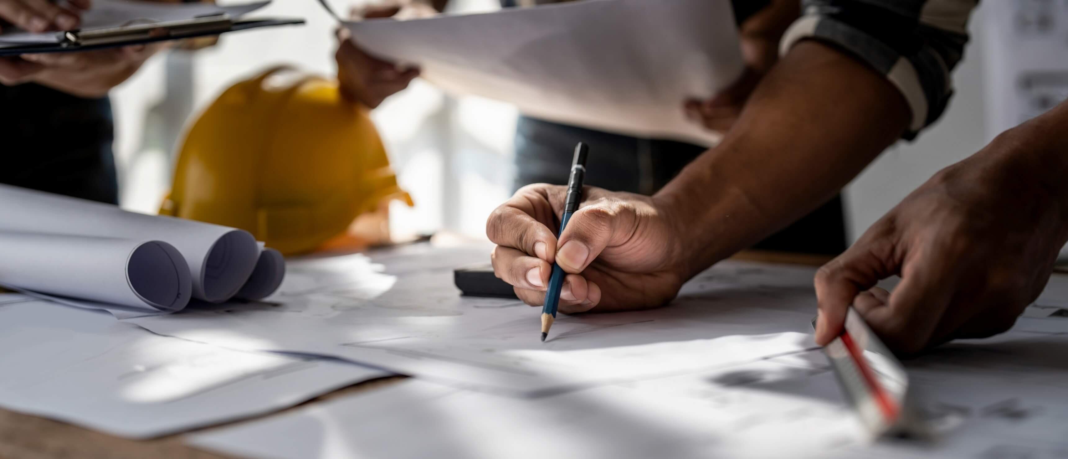 A close-up view of a team of three individuals, likely engineers or architects, collaborating around a table covered with blueprints and documents.